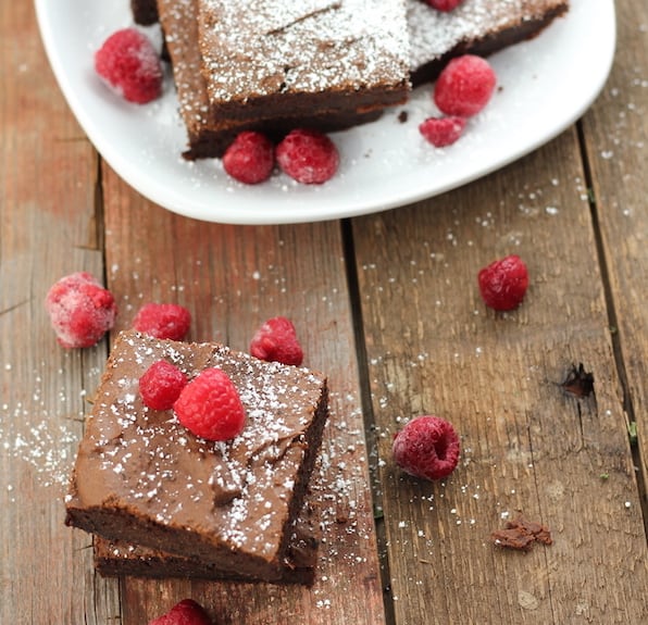 Image shows a plate of paleo brownies, along with a few brownies on a table next to it