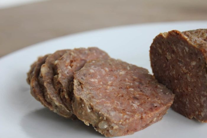 Slices of homemade summer sausage sit on a white plate