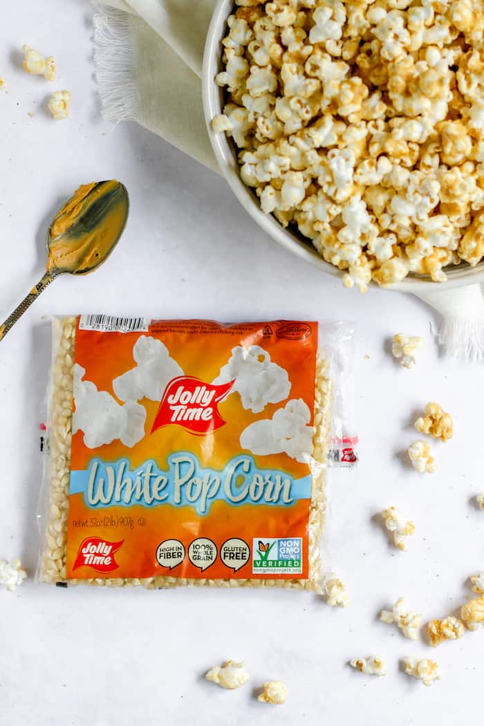 Image shows a bowl of peanut butter popcorn, next to a bag of Jolly Time White Popcorn and a spoon