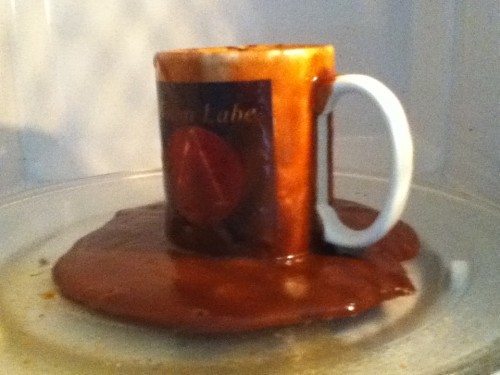 Image shows a coffee mug in a microwave with an overflow of black liquid covering the mug and tray