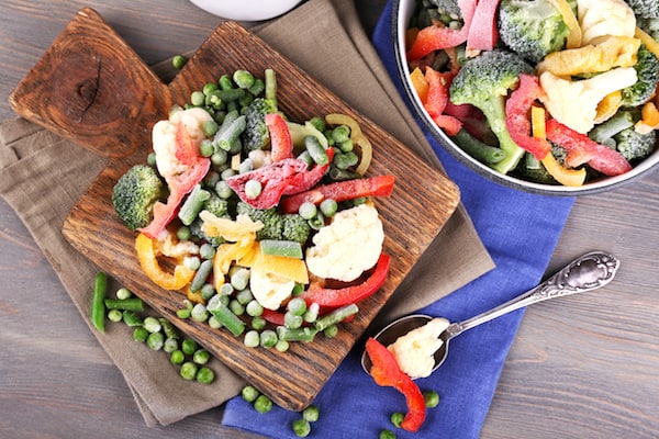 Image shows a cutting board with frozen veggies on a table
