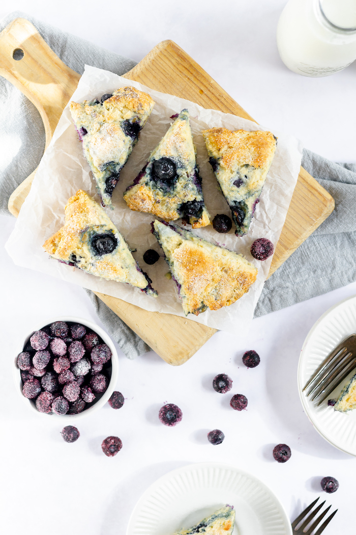 Photo shows blueberry scones on a cutting board next to a small bowl of blueberries