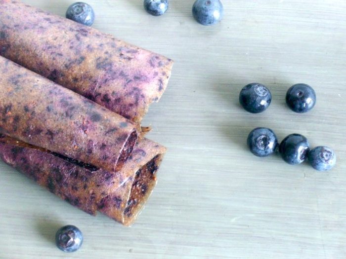 Photo shows three rolls of homemade fruit leather on a table with some blueberries