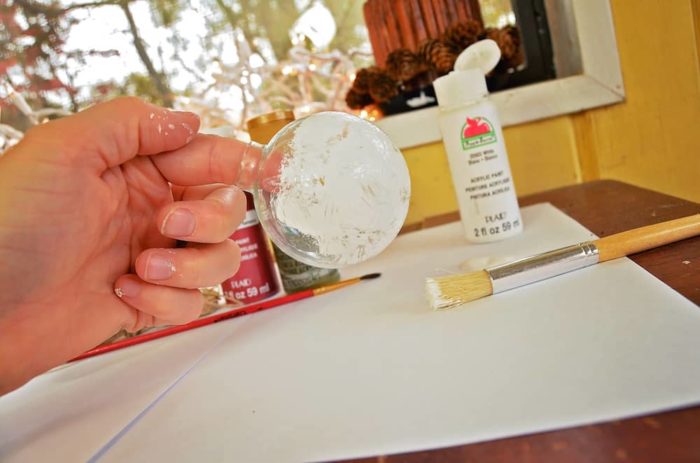 Photo shows a hand holding the glass ornament while painting it white