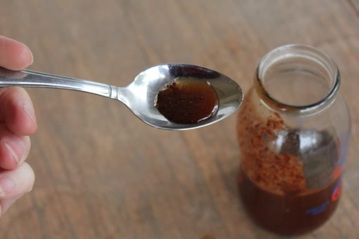 Image shows a spoon over a small jar holding homemade cough syrup
