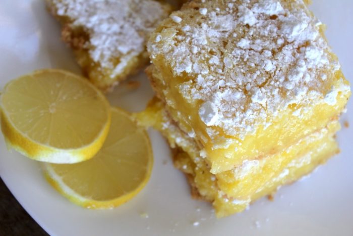 Photo shows a plate with several lemon bars with two slices of lemon