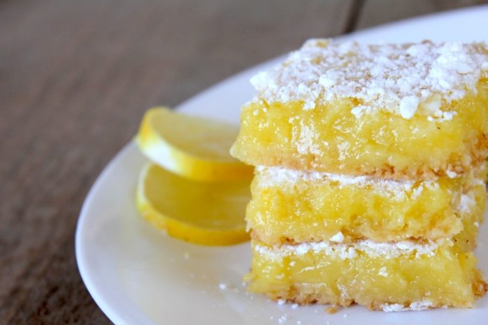 Image shows a plate of gluten-free lemon bars with two slices of lemon