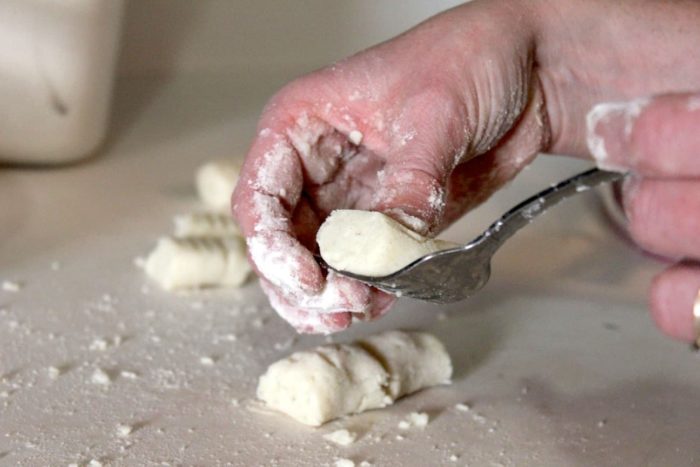 Image shows a hand rolling gnocchi on a fork