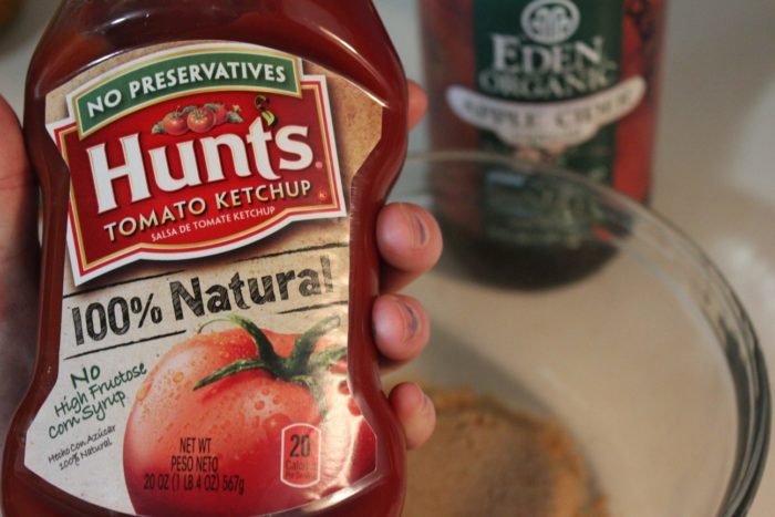 Photo shows a hand holding a bottle of Hunts Tomato Ketchup over a bowl