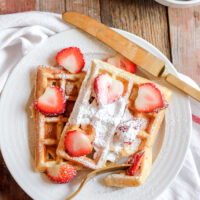 gluten free waffles with powdered sugar and strawberries on a plate.
