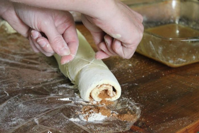 Photo shows two hands cutting the cinnamon roll with string