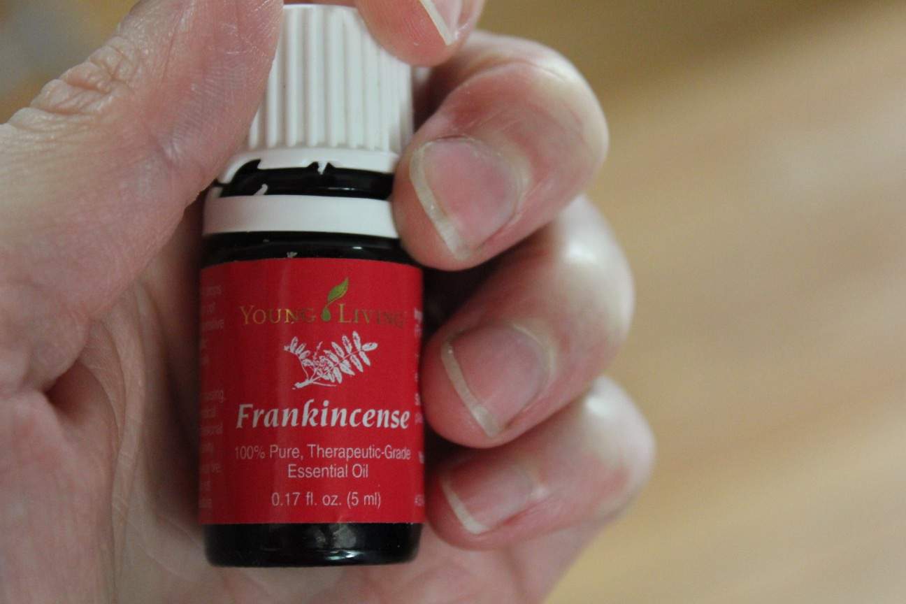 Image shows a close up of a hand holding a small bottle of Young Living Frankincense essential oil