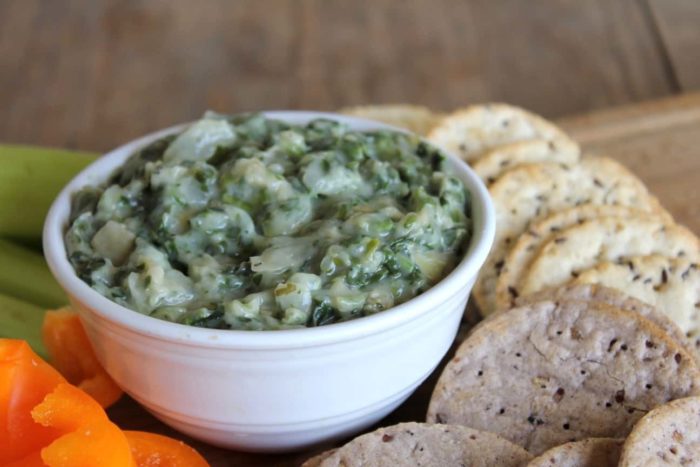 Photo shows a bowl of spinach and artichoke dip on a platter with crackers and veggies