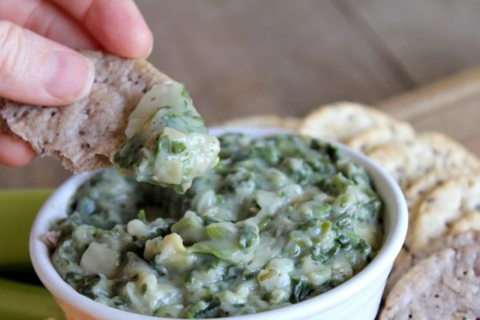Photo shows a hand dipping a cracker into a bowl of spinach artichoke dip