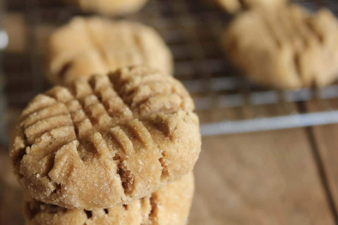 Image shows a close up of several peanut butter banana cookies with fork marks pressed into the top. In the background are more cookies cooling on a cooling rack