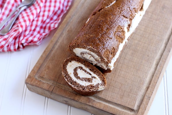 Image shows a pumpkin roll on a wooden cutting board