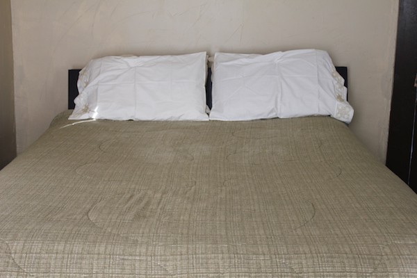Image shows a photo of a bed with white pillowcases and a grey comforter
