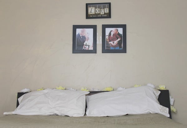 Photo shows a bed with a floral garland across the headboard, and photos displayed on the wall