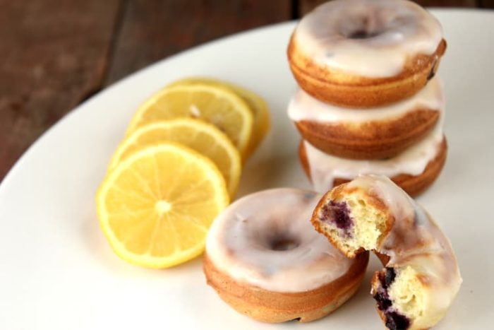 Image shows several blueberry doughnuts stacked on a plate next to several slices of lemon