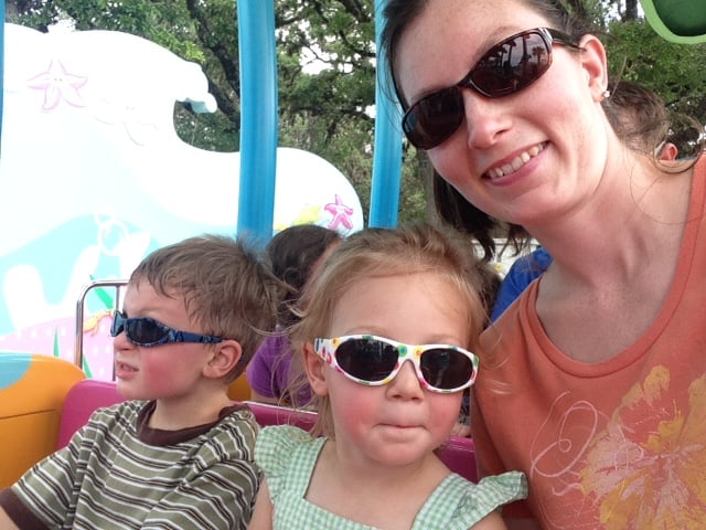 Image shows two small children outdoors with a woman, all wearing sunglasses