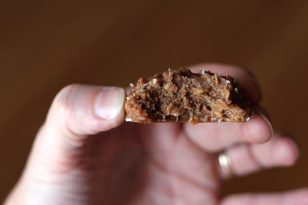 Photo shows a hand holding a no-bake almond cookie with a bite taken out of it