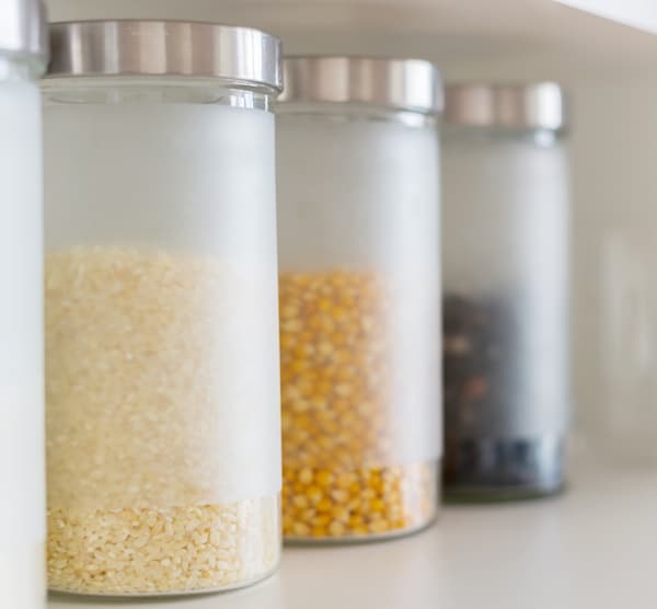 Image shows several glass jars on a shelf full of various grains, including rice and corn. 