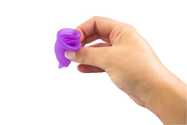 Image shows a hand holding a folded purple menstrual cup
