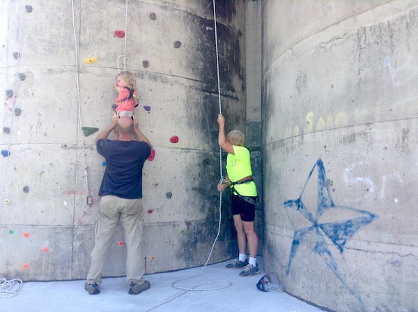Photo shows a man helping a small child climb on a rock wall