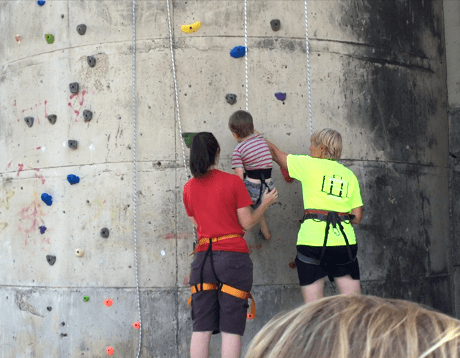 Image shows a woman helping a young child on a rock climbing wall
