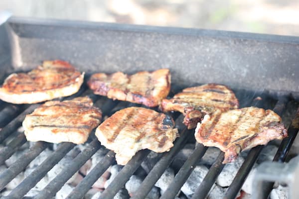 Image shows several pieces of pork cooking on the grill