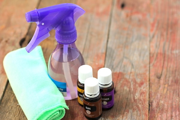 Photo shows a purple spray bottle sitting on a table with a rolled up cloth and three small bottles of essential oil nearby. 