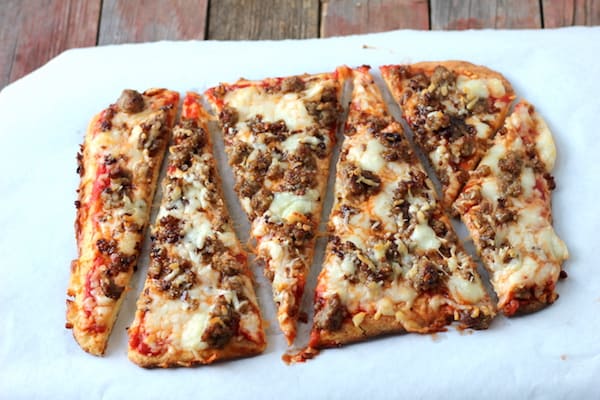 Photo shows a rectangle sausage pizza on parchment paper sliced into large triangles