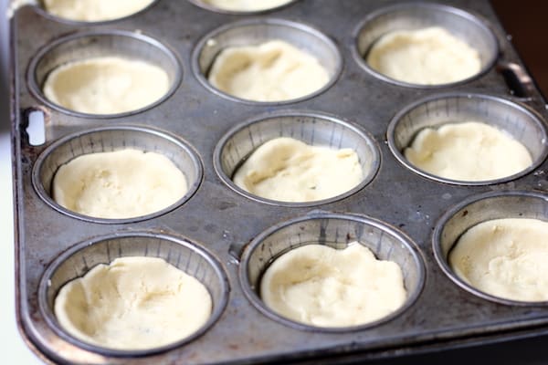 Image shows a muffin tin with pizza crusts ready to bake