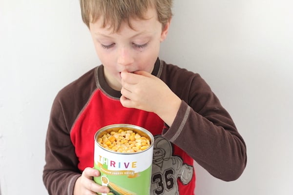 Image shows a young boy eating corn from a can 