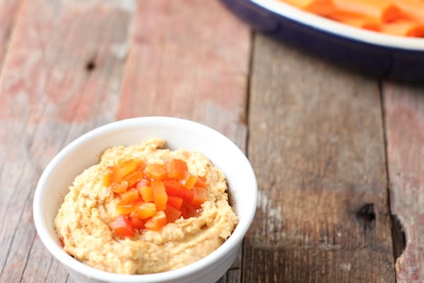 Image shows a small bowl of garlic and roasted red pepper hummus on a table