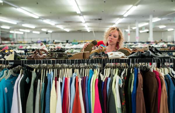 Image shows a woman in a thrift shop at a rack of clothes