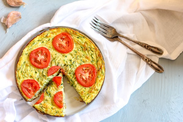 Image depicts a pan of zucchini frittata on a white napkin next to two forks