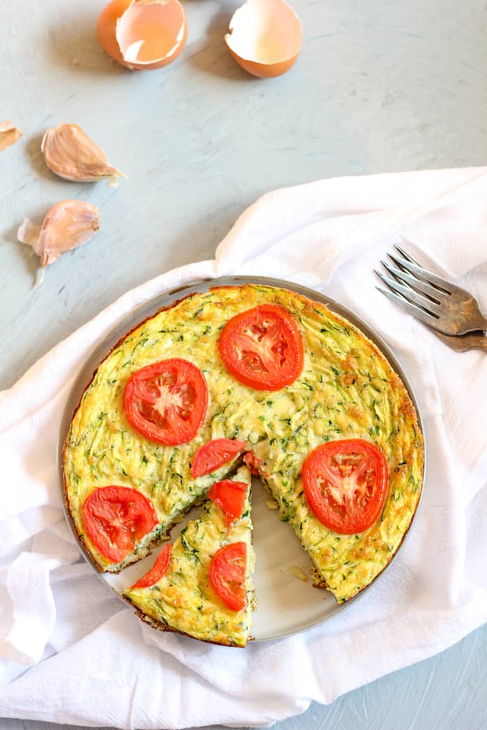 Image shows a dish of zucchini frittata on a white napkin next to a fork