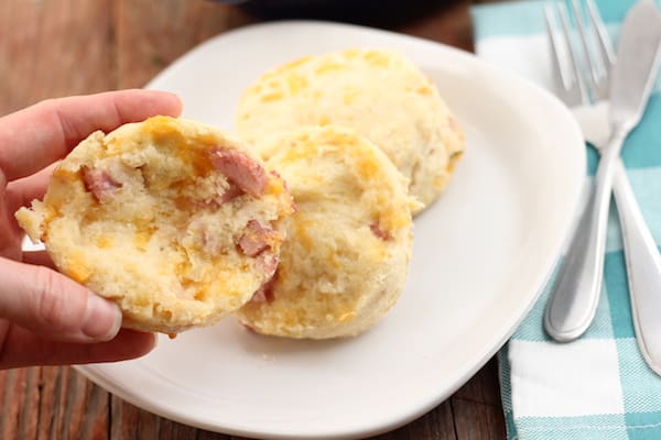 Photo shows a hand holding half a ham and cheese biscuit over a plate