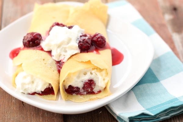 Image shows two fresh crepes on a plate with fresh blackberries