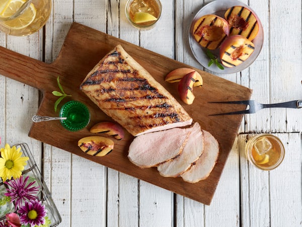 Image shows grilled pork loin with a few slices cut off on a table, photographed from above