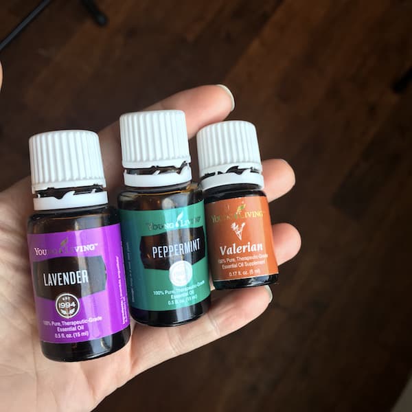 Image shows a hand holding three small bottles of Young Living Lavender, Peppermint and Valerian essential oils. 