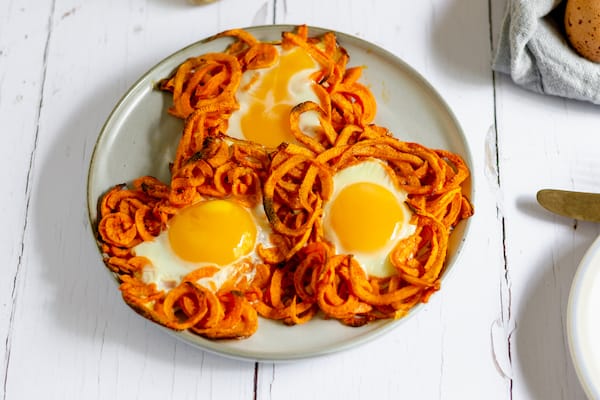 Image shows a plate of three sweet potato "nests" with cooked eggs in the center