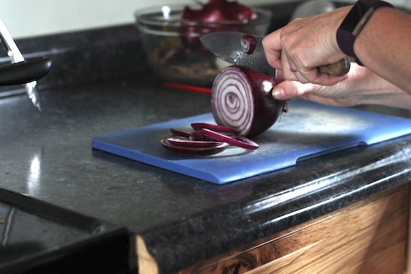 Image shows a hand cutting a red onion on a blue cutting board