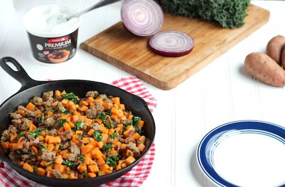 Photo shows a cast iron skillet with sweet potato hash on a table, next to an emply blue and white plate