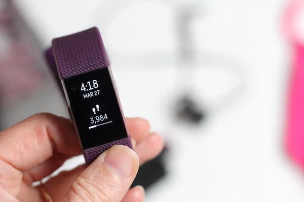 Image shows a hand holding a purple FitBit