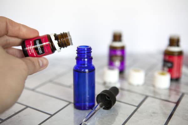 Image shows a hand pouring an essential oil into a blue bottle