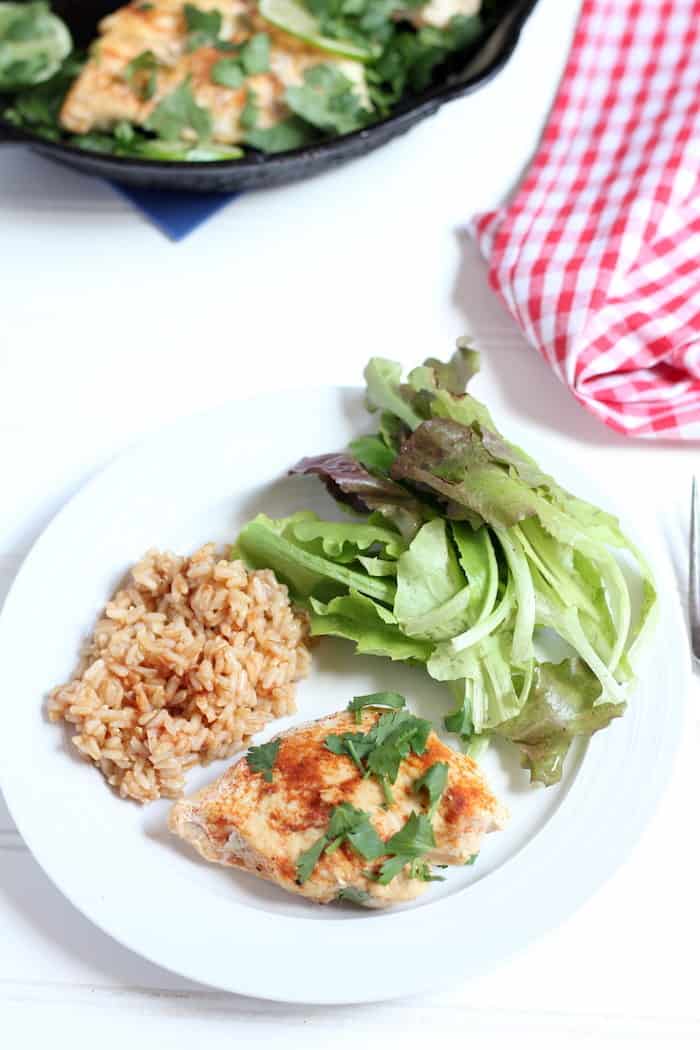 Image shows a plate with chicken, rice and greens on a table 
