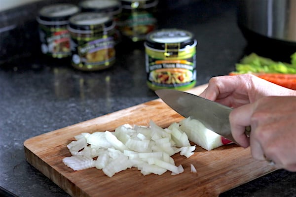 Image shows a hand chopping onions on a chopping board