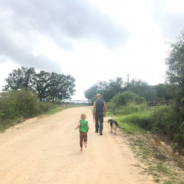 Image shows a man, dog, and small child walking down a dirt road